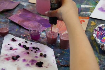 Ein Kinderarm mit einem Pinsel in der Hand und Naturfarben in lila