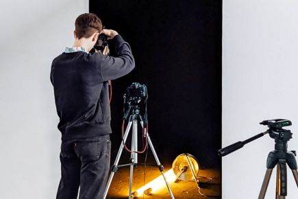 Eine Person von hinten, die mit einer Digitalkamera einen dunklen Raum mit Neonlicht fotografiert